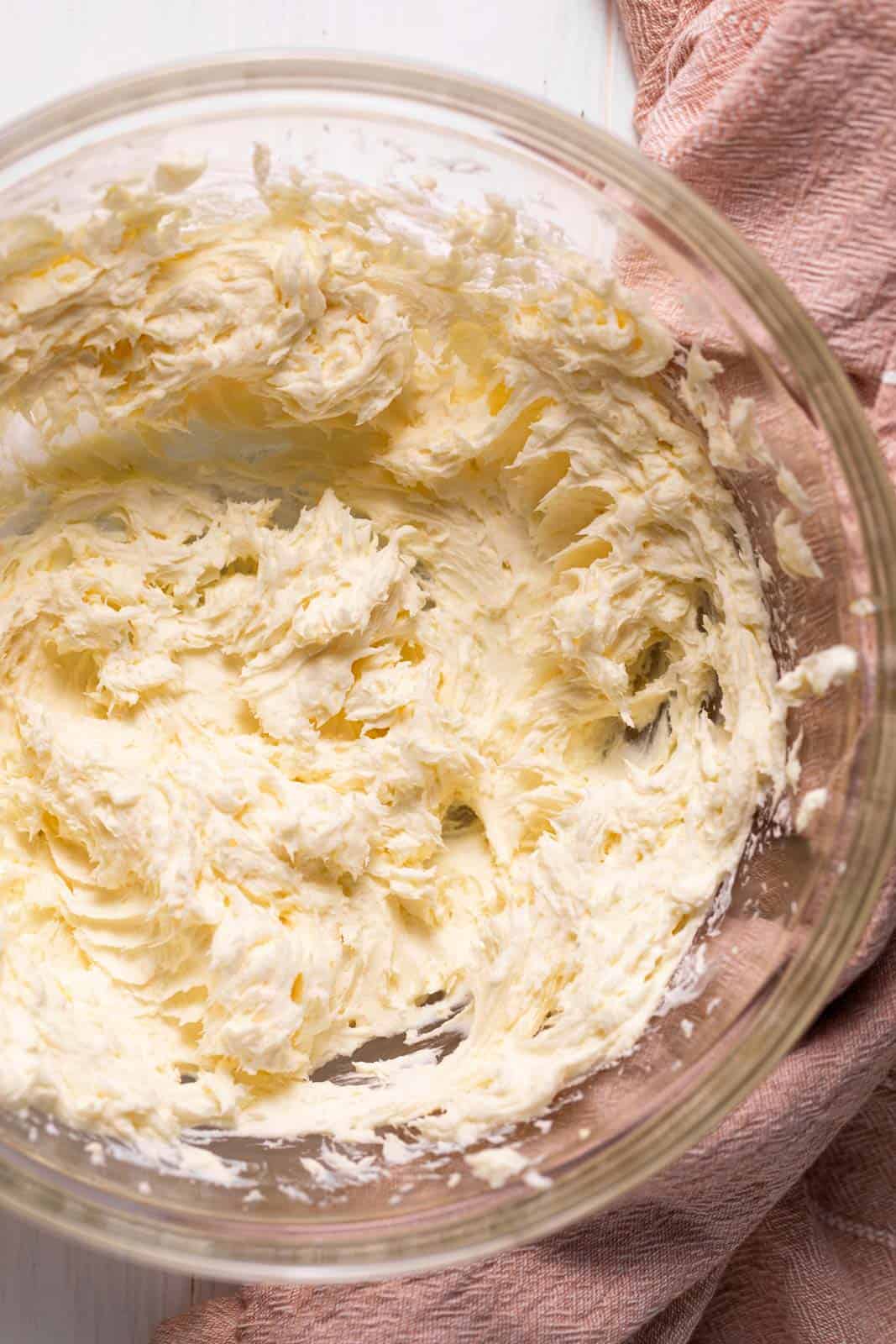 Creamed butter and cream cheese in a glass bowl set on a pink towel.