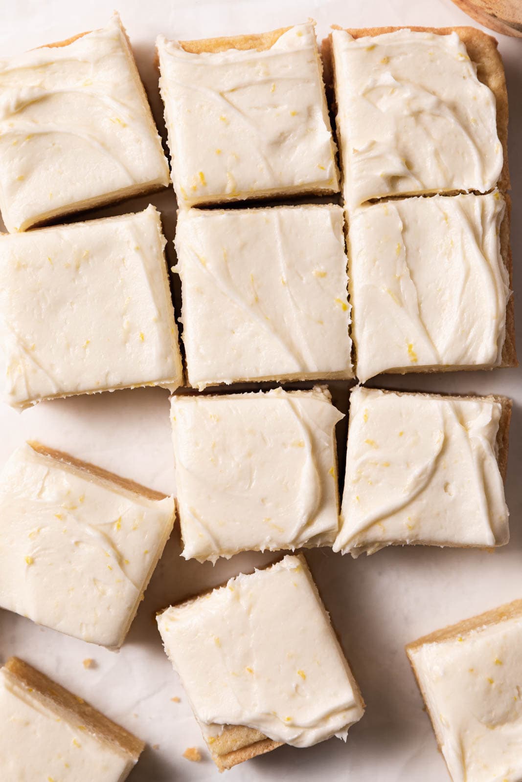 Lemon cream cheese frosting spread over sugar cookie bars cut into squares.