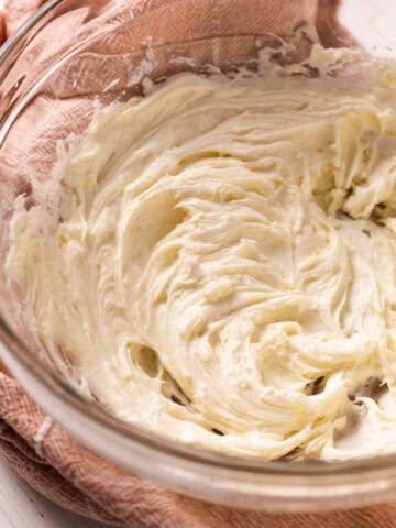 Lemon cream cheese frosting in a glass mixing bowl set on a pink towel.