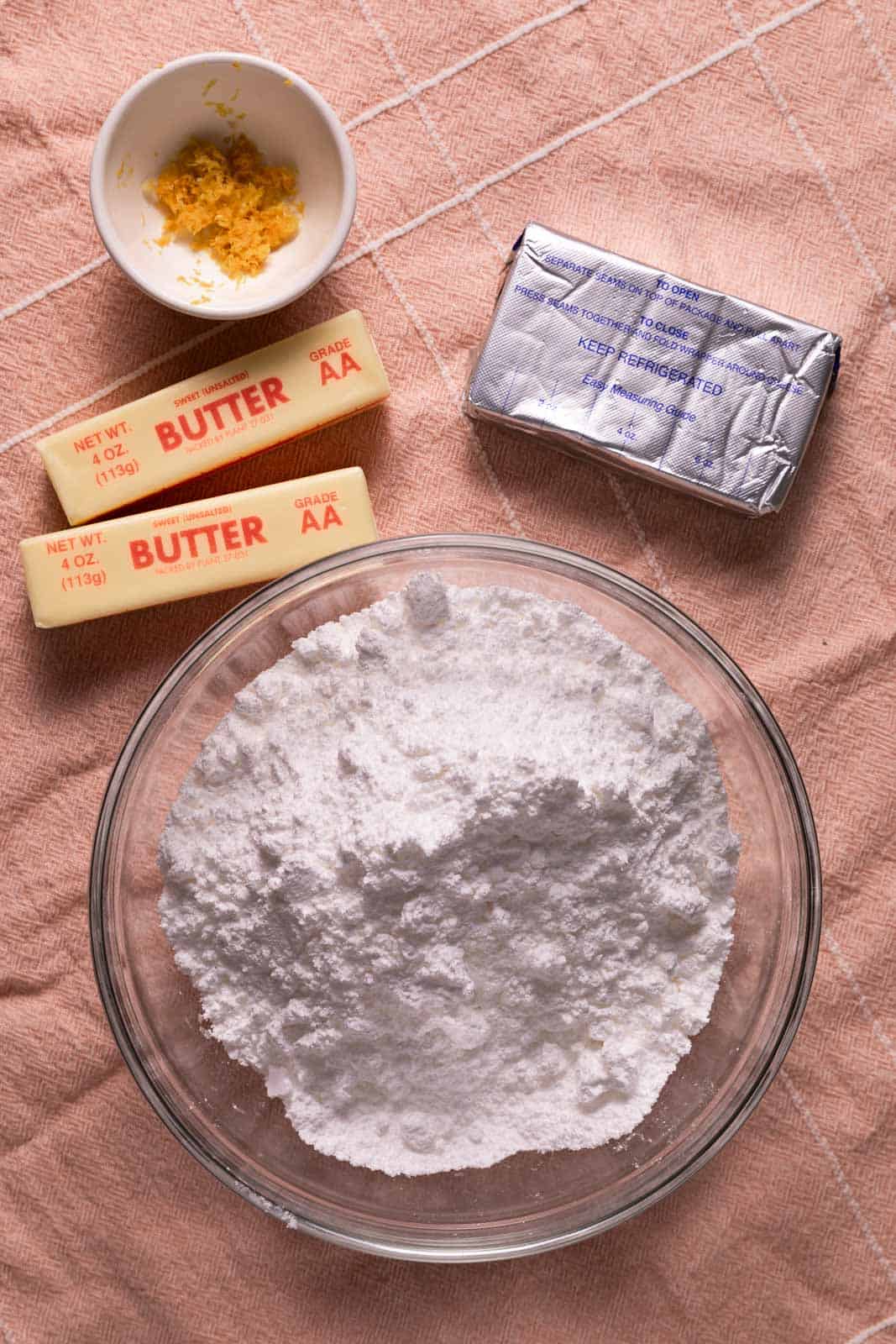 Ingredients for lemon cream cheese frosting set on a pink towel.