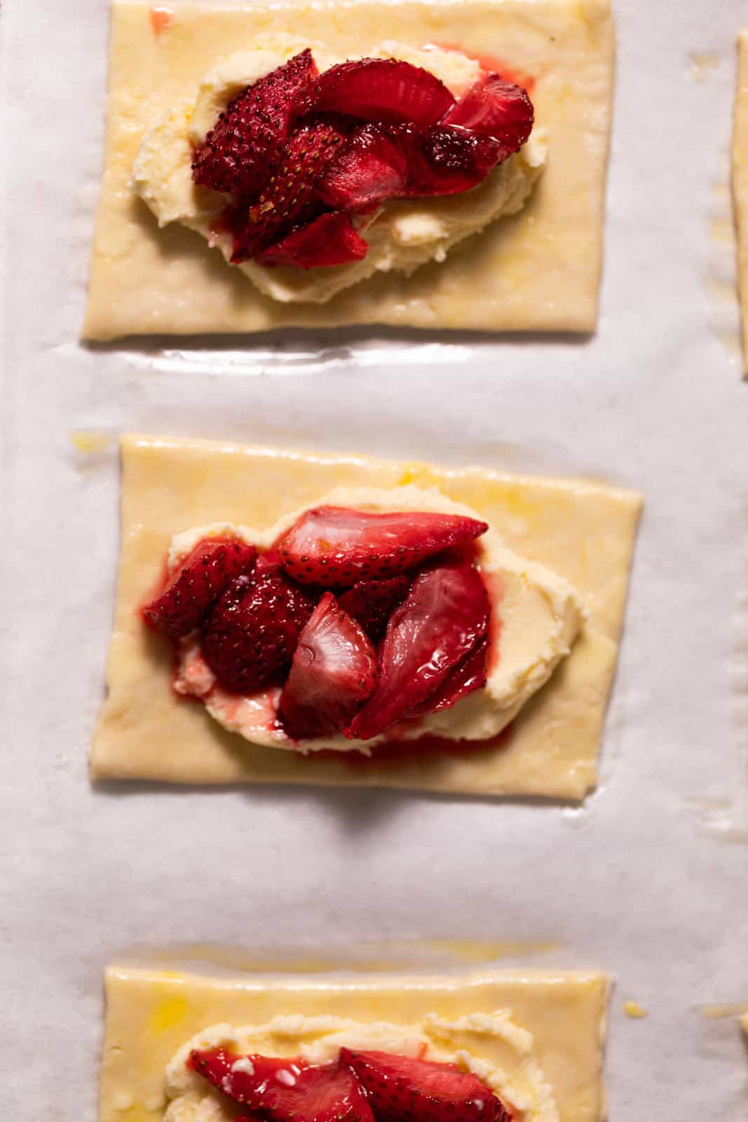 Pie dough topped with mascarpone cheese and roasted strawberries on a parchment lined sheet pan.