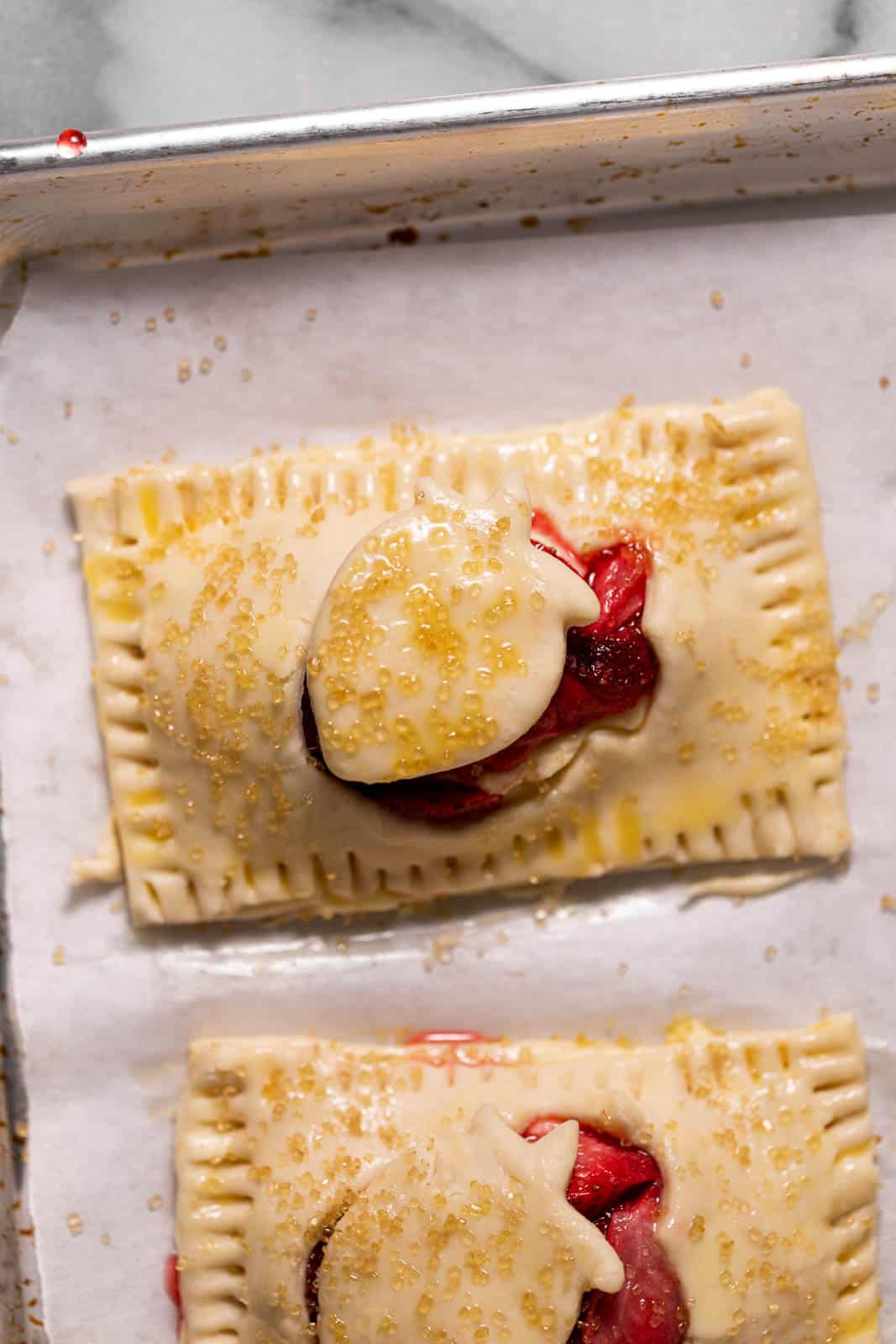 Unbaked strawberry handpies sprinkled with coarse sugar and set on a parchment lined sheet pan.