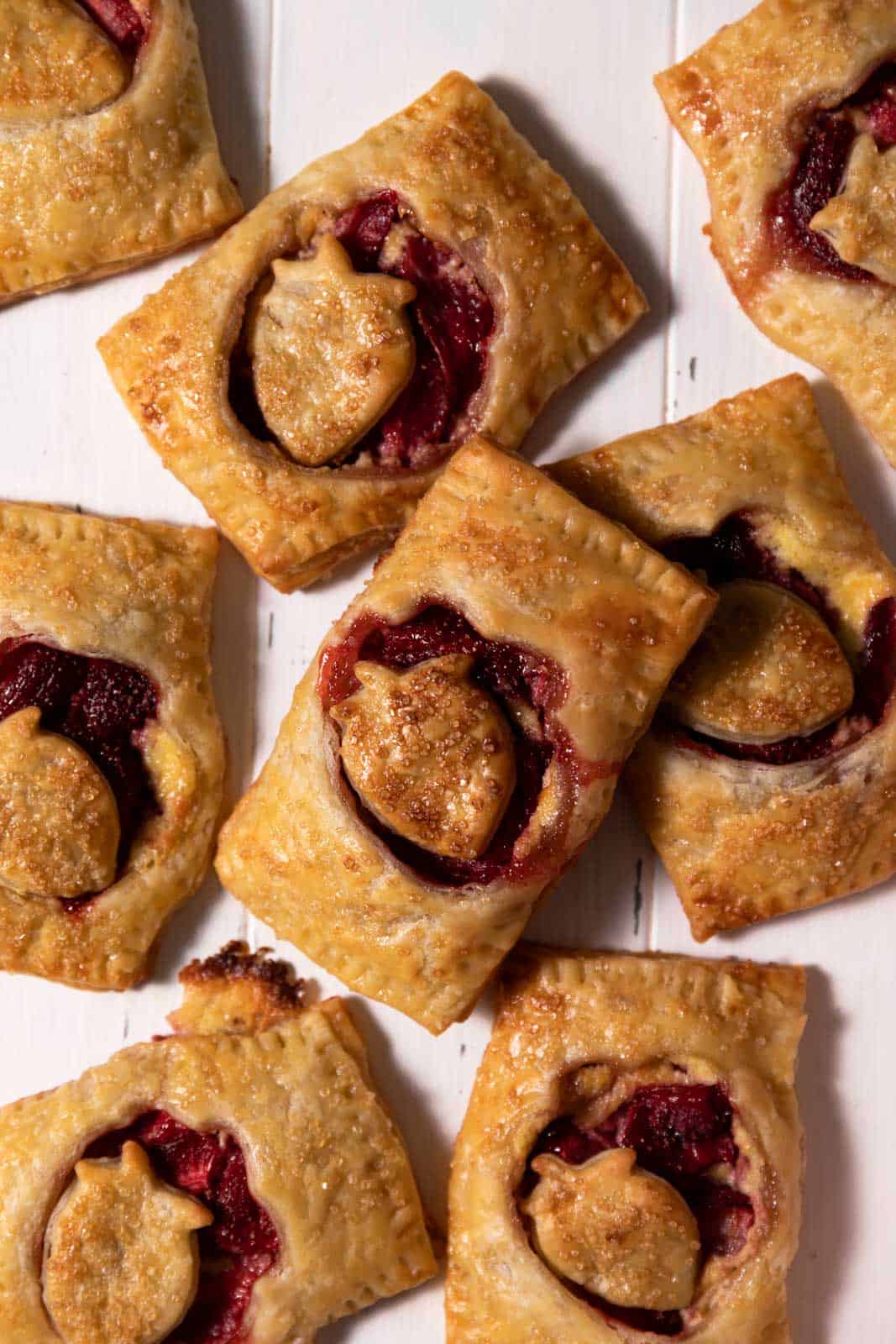 Randomly arranged toasted strawberry hand pies on white wood.