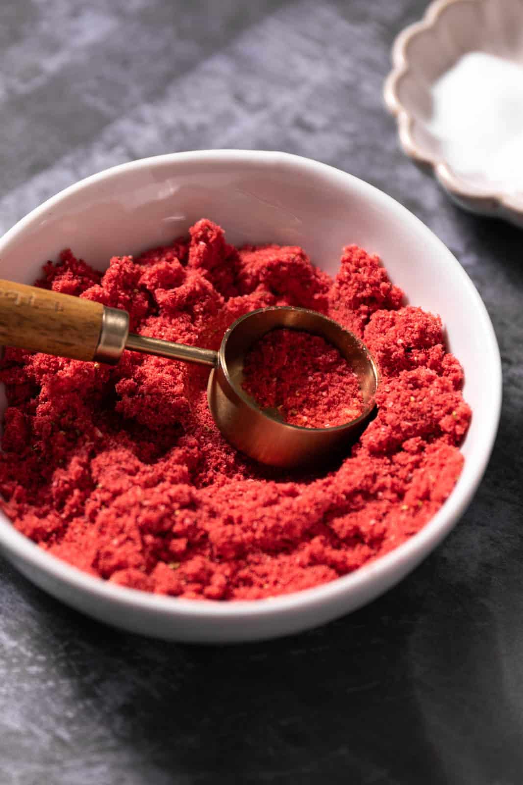 Freeze-dried strawberry powder in a white bowl with a gold measuring spoon.