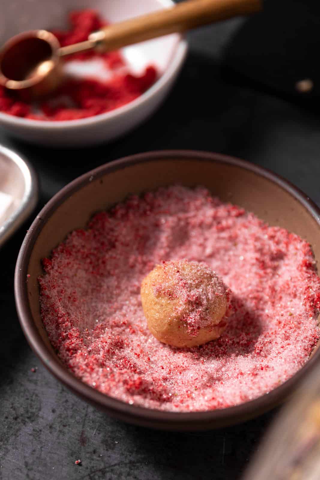Strawberry sugar cookie dough ball in a bowl of strawberry sugar.