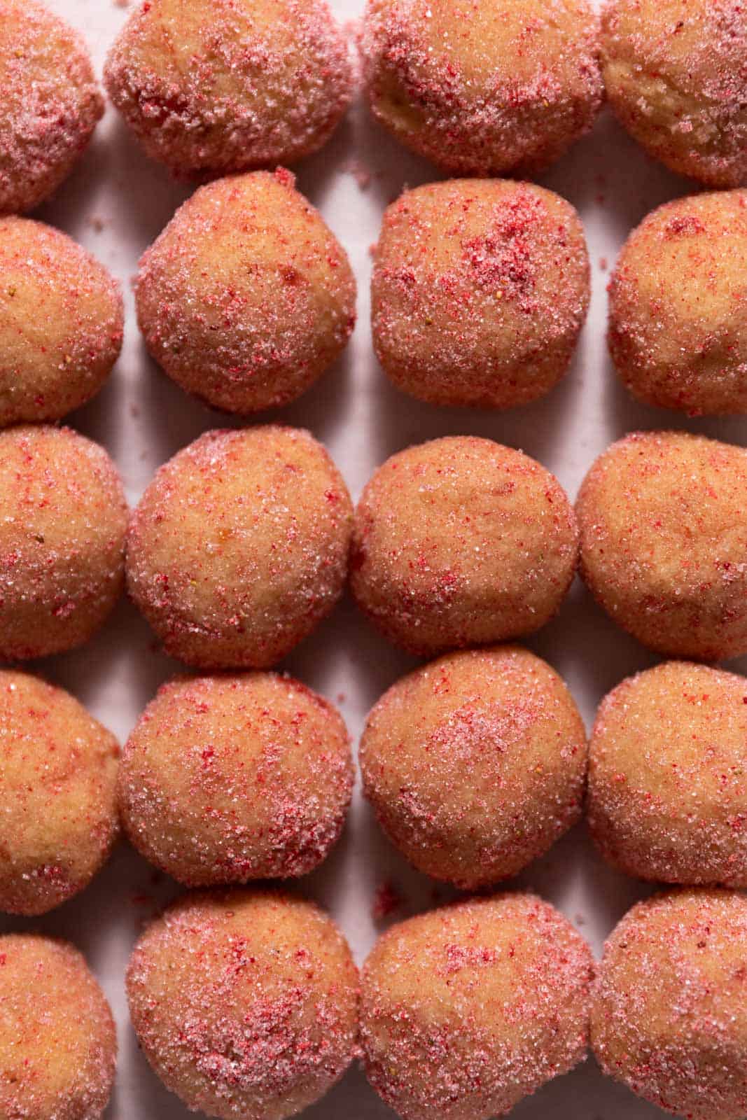 Strawberry sugar cookie dough balls rolls in strawberry sugar on a parchment lined sheet pan.