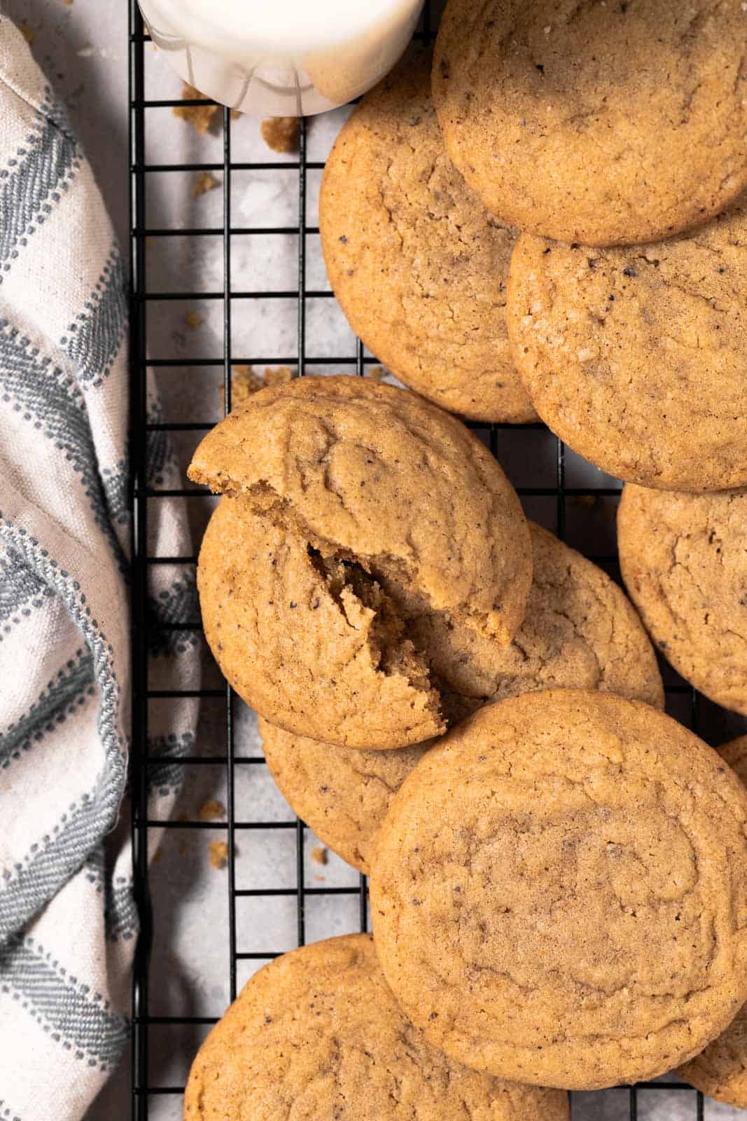 Brown butter chocolate chipless cookies arranged on a black cooling rack with a cookie broken in half.