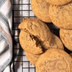 Brown butter chocolate chipless cookies arranged on a black cooling rack with a cookie broken in half.