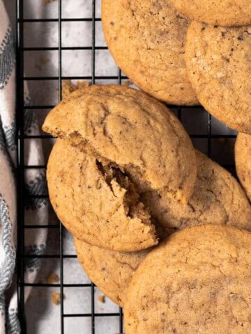 Brown butter chocolate chipless cookies arranged on a black cooling rack with a cookie broken in half.