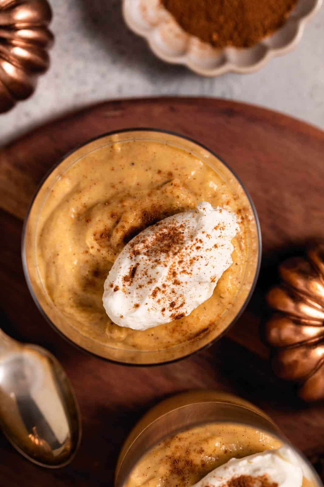 Overhead shot of glass with pumpkin custard with a dollop of whipped cream and pumpkin pie spice.