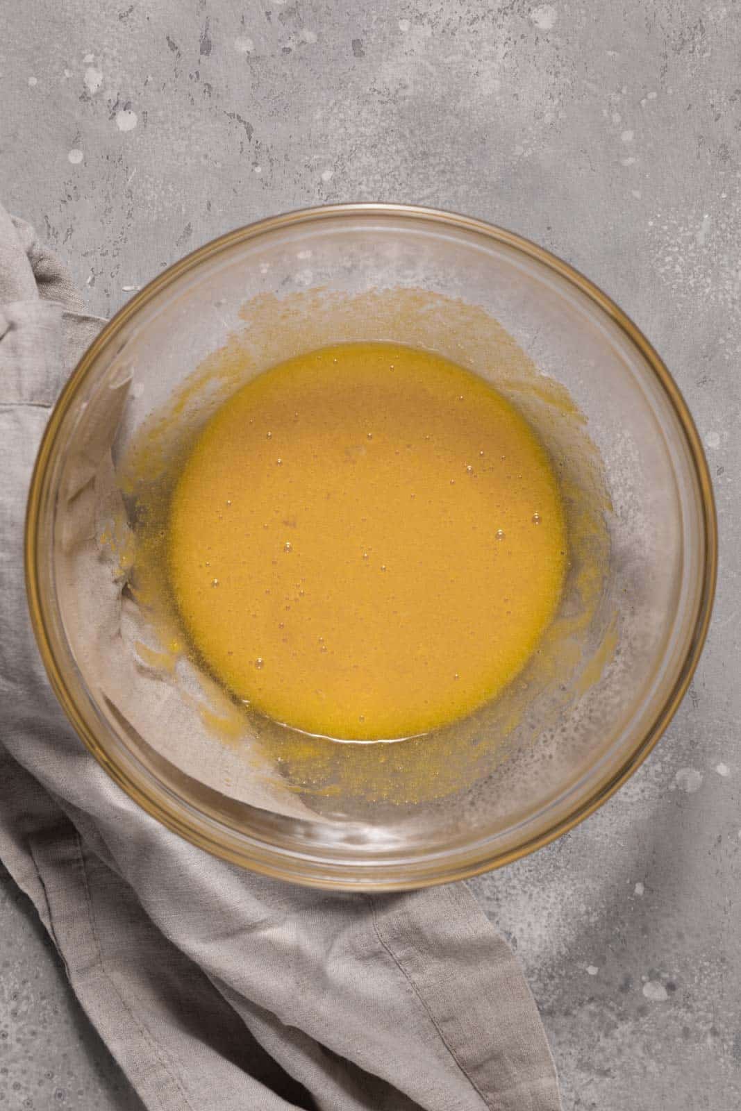 Whisked eggs and sugar in a glass mixing bowl set on a flat surface.
