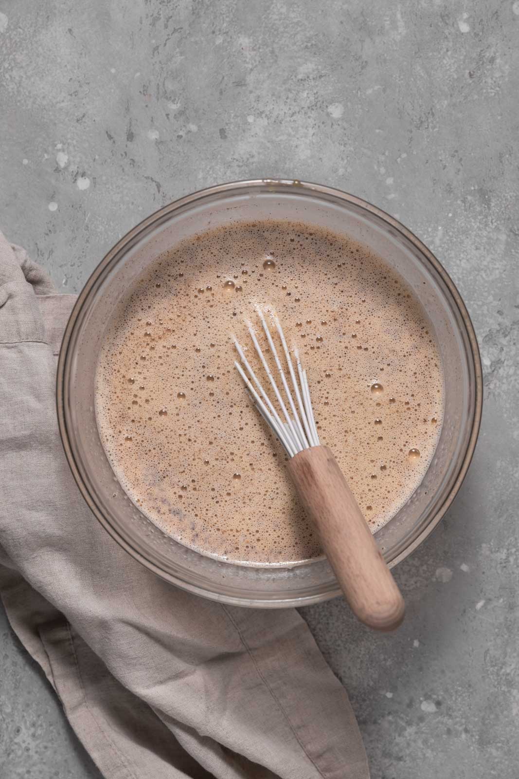 Whisked custard mixture with pumpkin in a glass mixing bowl set on a flat surface.