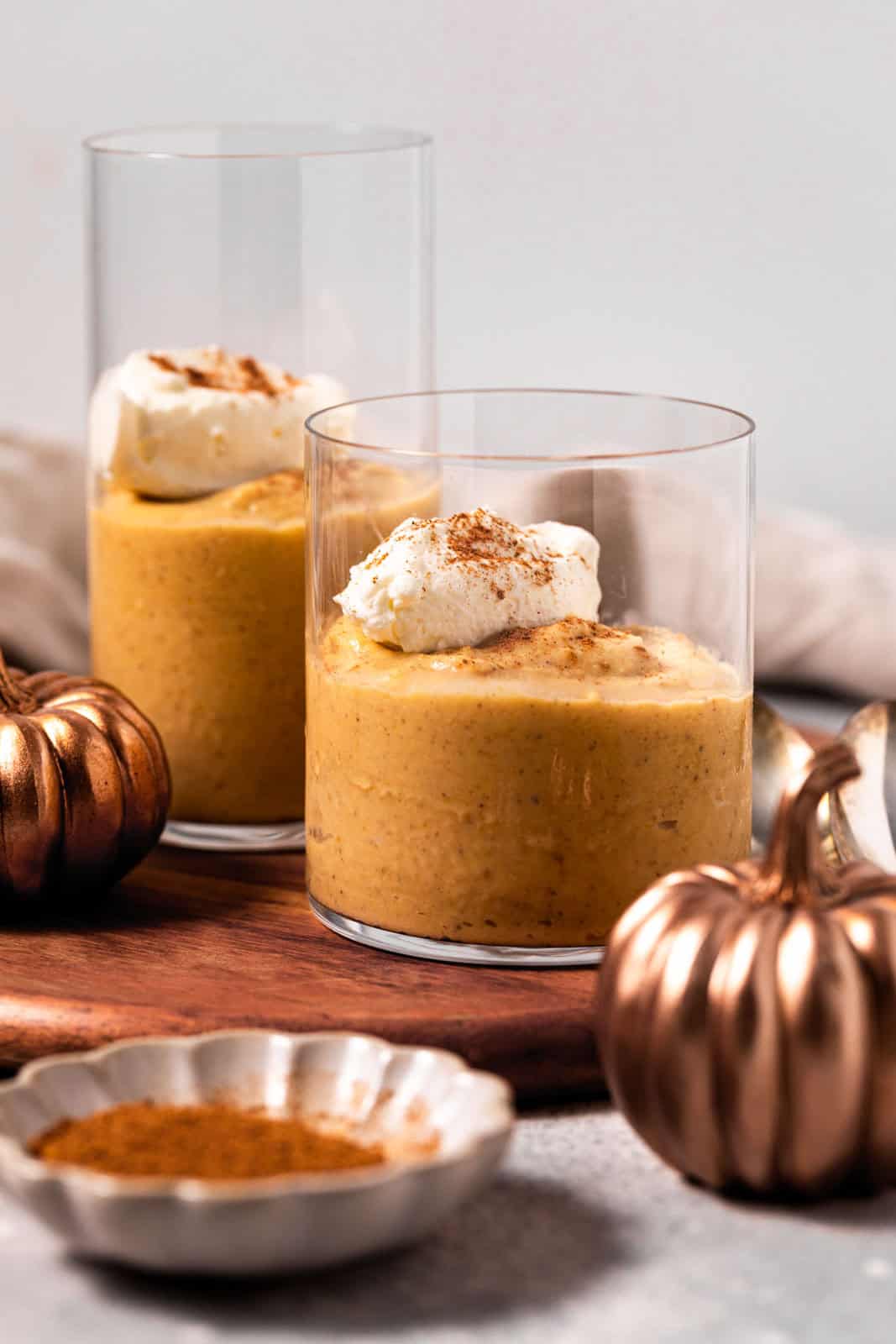 Pumpkin custard in glasses with a dollop of whipped cream set on a wood board.