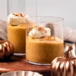 Pumpkin custard in glasses with a dollop of whipped cream set on a wood board.