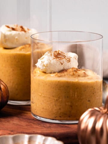 Pumpkin custard in glasses with a dollop of whipped cream set on a wood board.