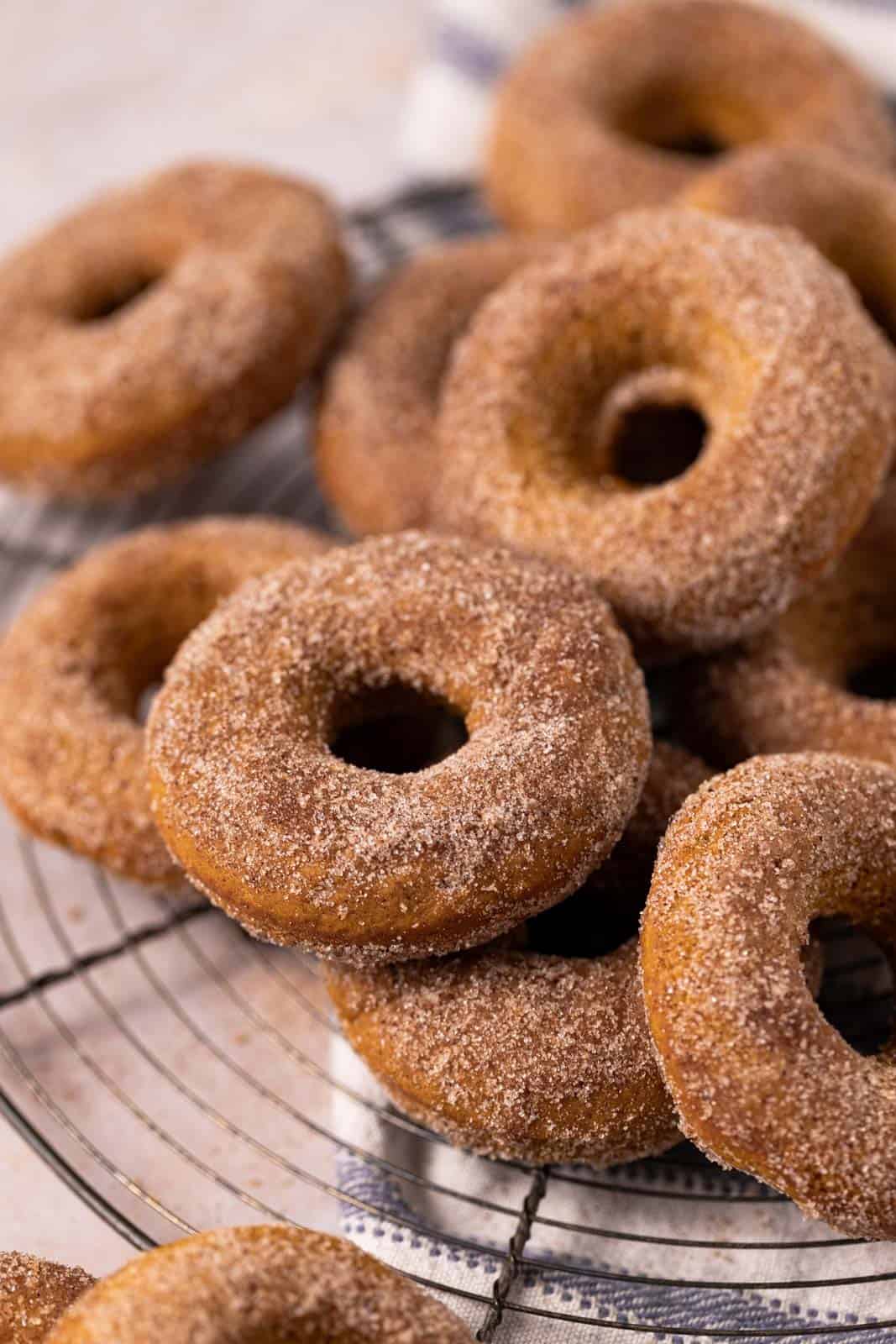 Close up of baked pumpkin donuts stacked on a round wire cooling rack.
