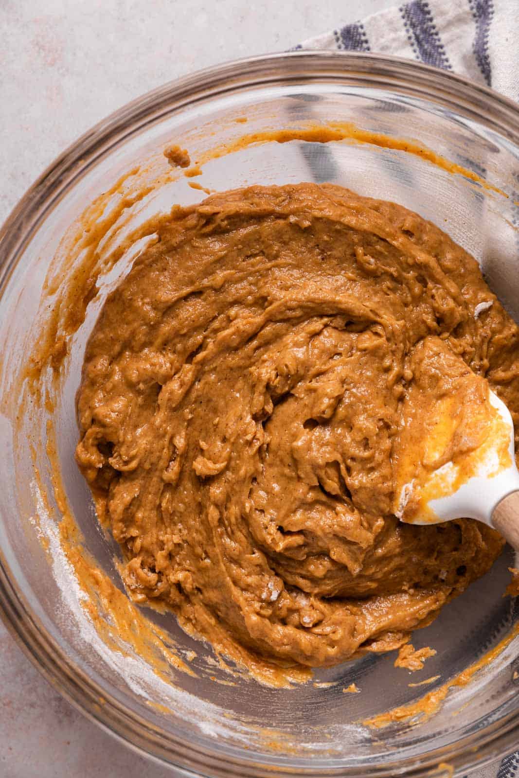 Pumpkin donuts batter in a glass mixing bowl with a white rubber spatula.