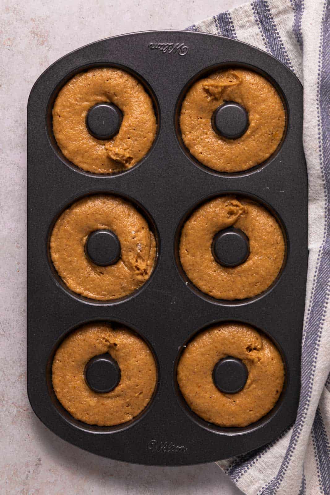 Pumpkin donut batter piped into a donut pan for baking.