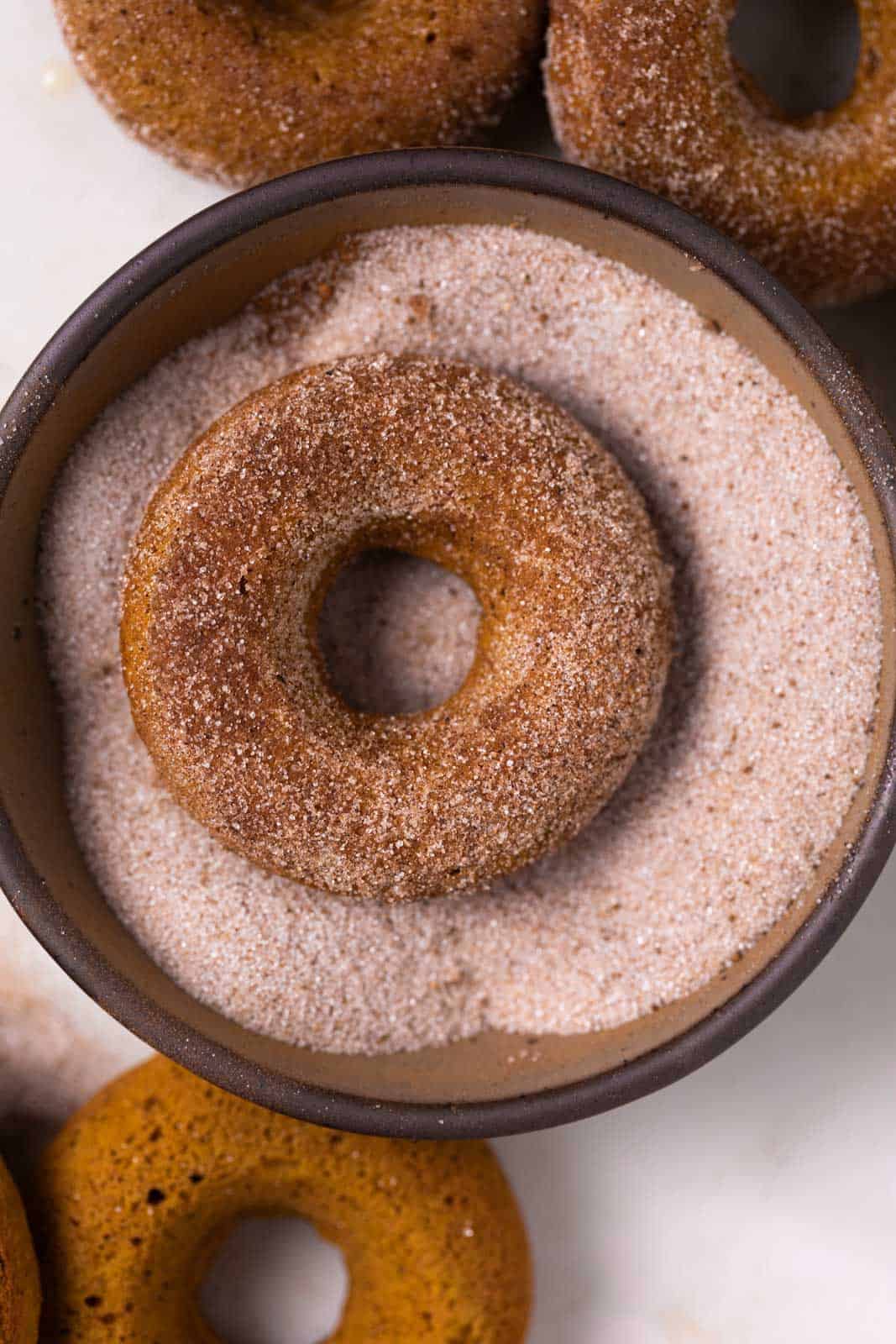 Pumpkin donuts in a bowl of pumpkin pie spice sugar for coating.