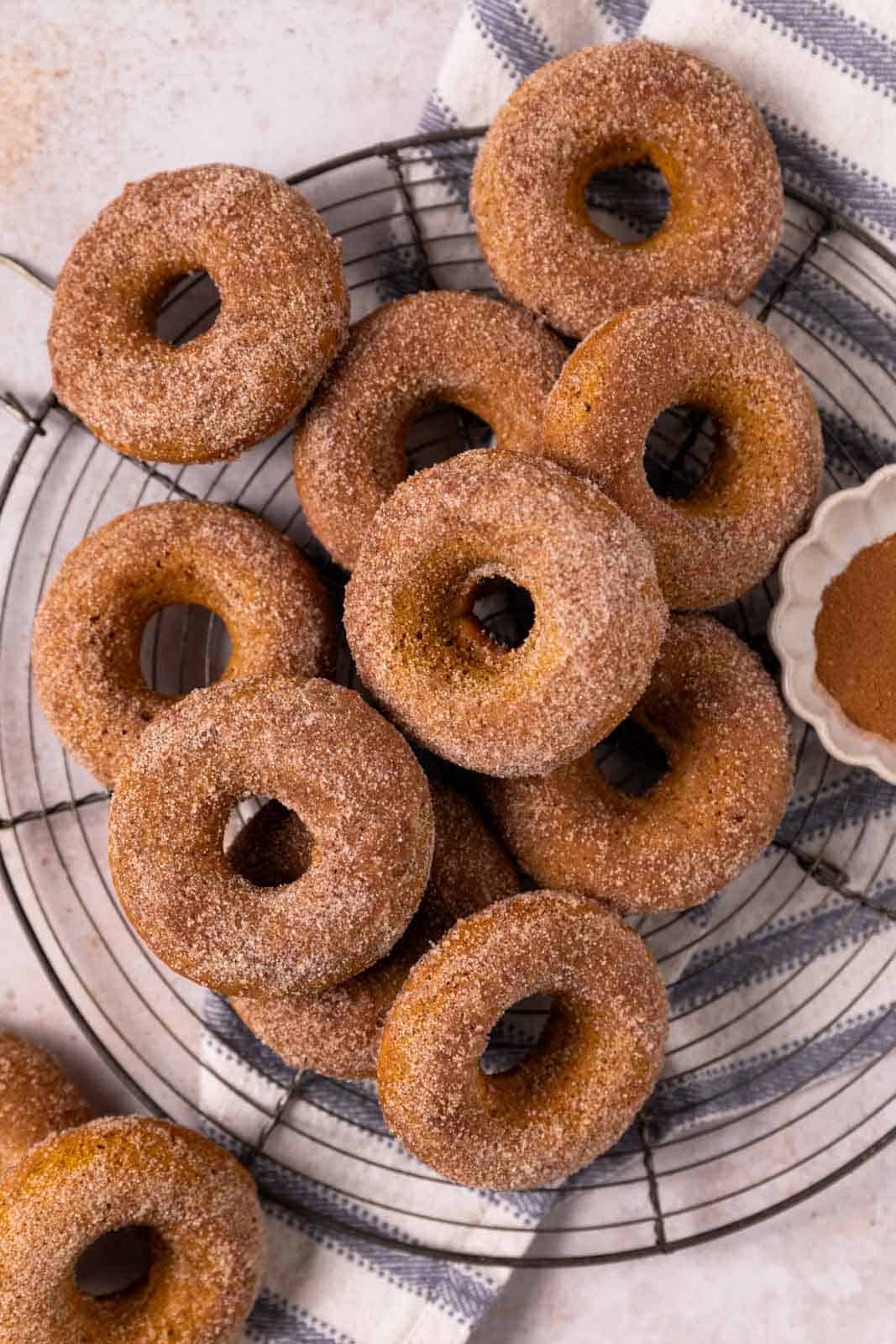 Overhead shot of baked pumpkin donuts stacked on a round wire cooling rack.