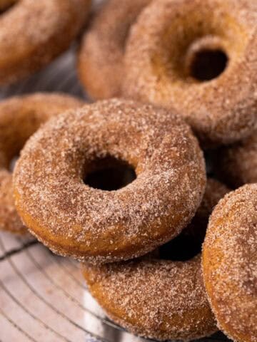 Close up of baked pumpkin donuts stacked on a round wire cooling rack.