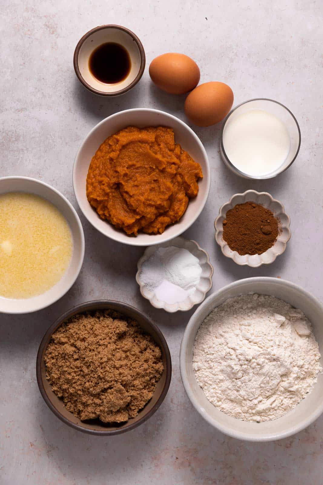 Ingredients for pumpkin donuts in bowls set on a flat surface.
