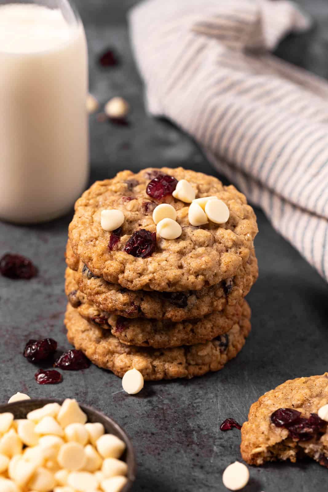 Stack of white chocolate cranberry oatmeal cookies on a flat surface with milk and a linen.