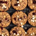 White chocolate cranberry oatmeal cookies in a single layer on a black wire cooling rack.