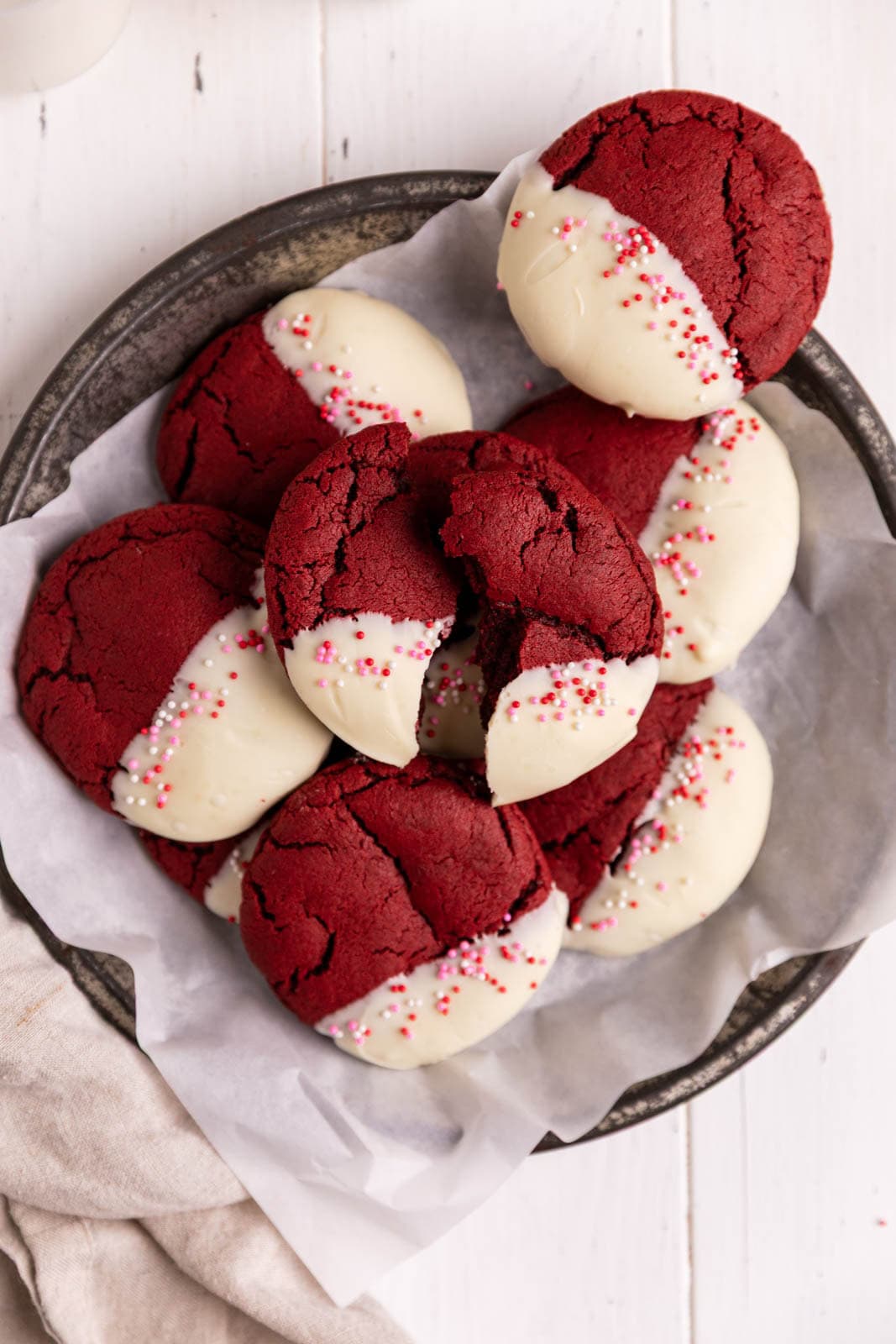 Red velvet cookies dipped in white chocolate and arranged in a parchment lined metal pie tin.