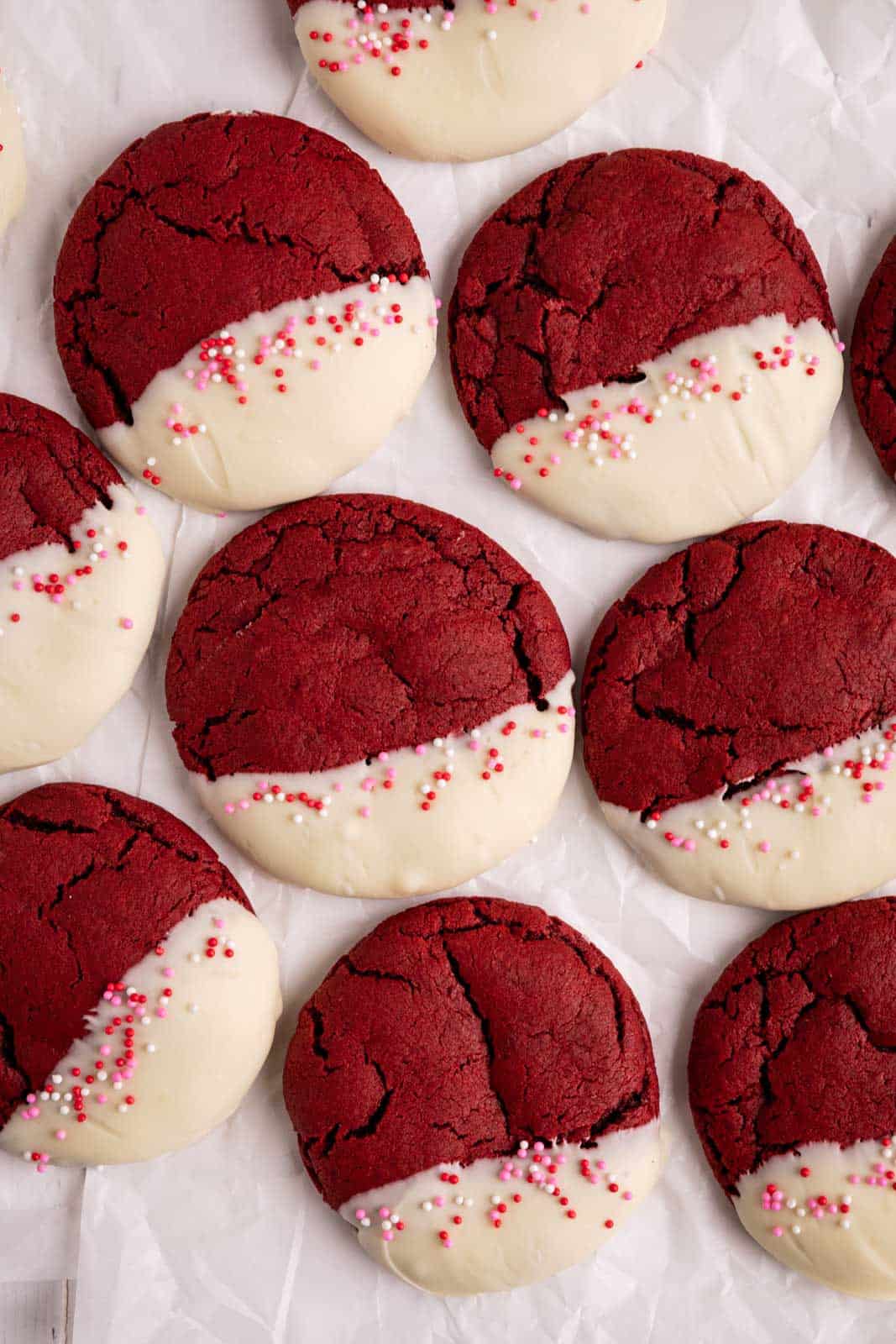 Overhead shot of red velvet cookies dipped in white chocolate on a parchment sheet surface.