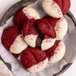 Red velvet cookies dipped in white chocolate and arranged in a parchment lined metal pie tin.