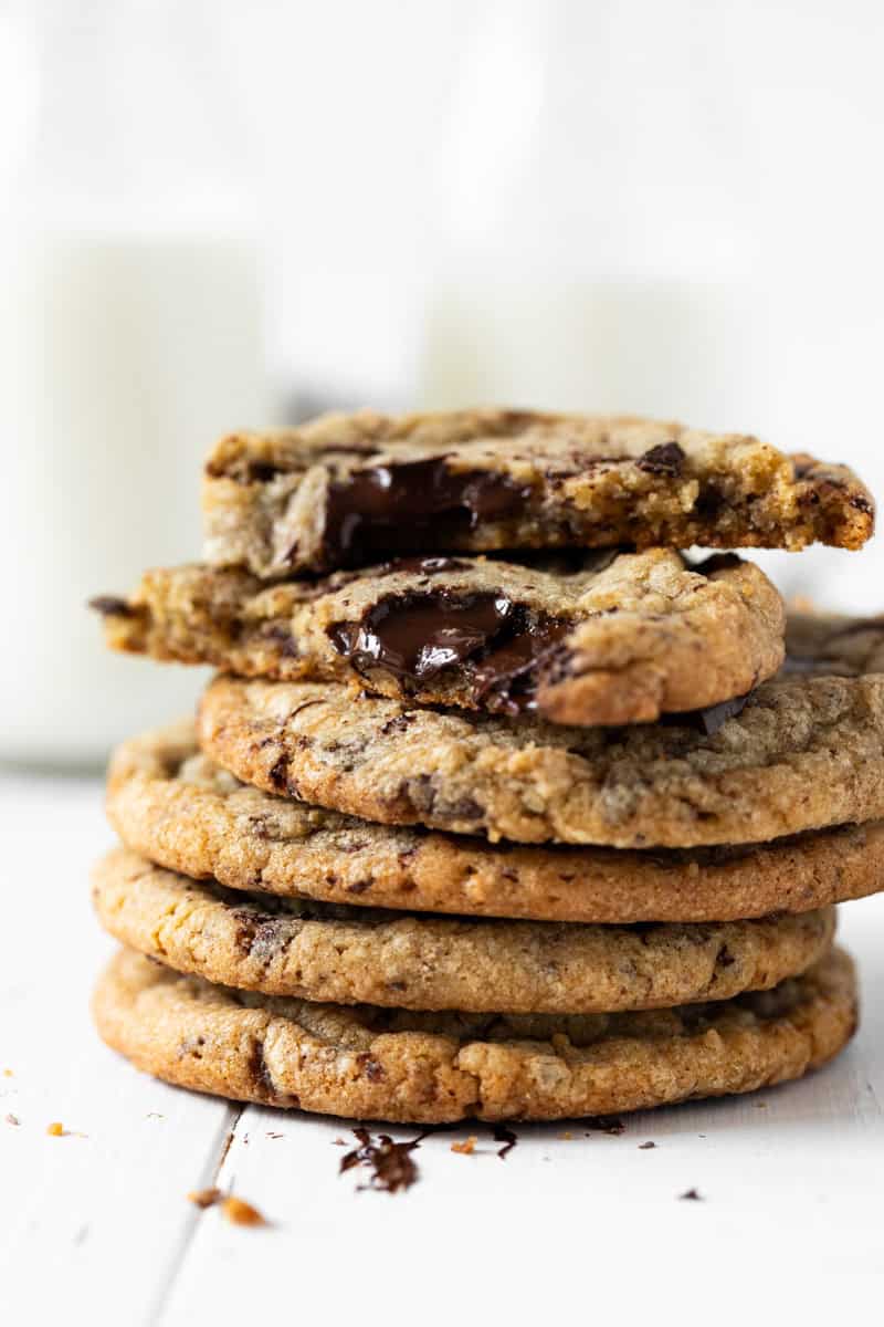 Stack of chewy chocolate chip cookies on a white wood board with the top cookie cut in have with melted chocolate showing.