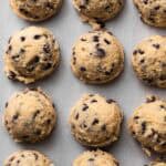 Edible chocolate chip cookie dough scooped and spaced out in rows on a parchment-lined sheet pan.