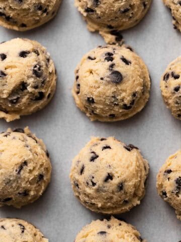 Edible chocolate chip cookie dough scooped and spaced out in rows on a parchment-lined sheet pan.