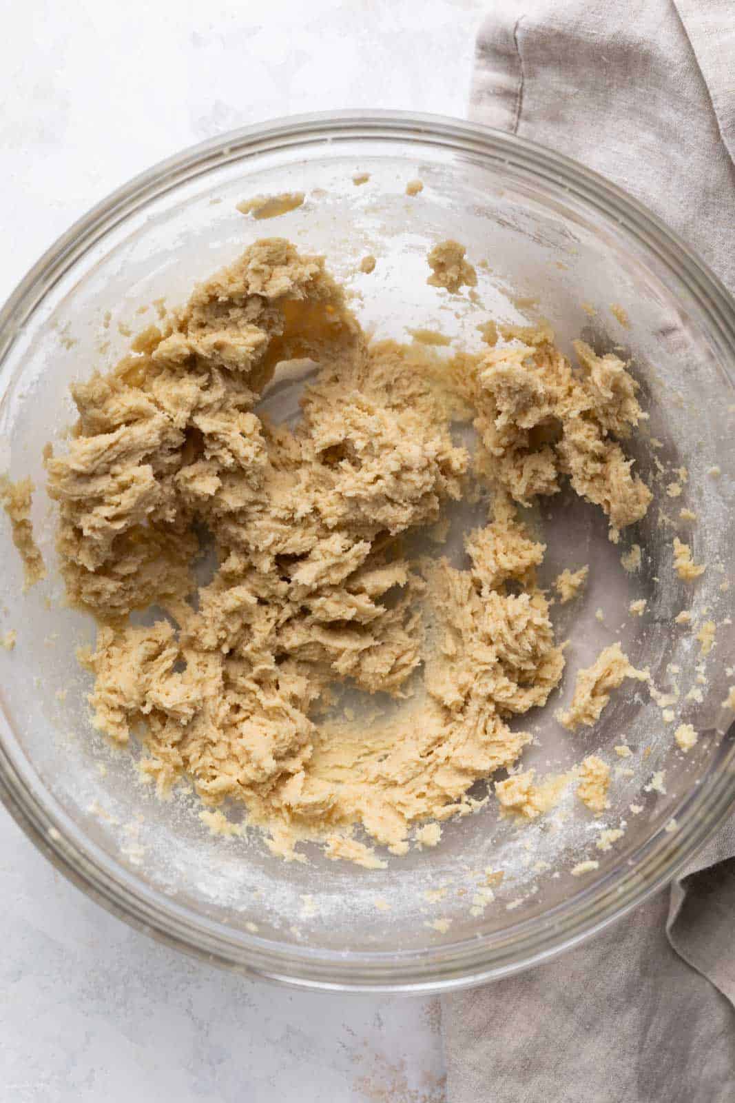 Creamed butter and sugar mixed with flour in a glass mixing bowl set on a flat surface.