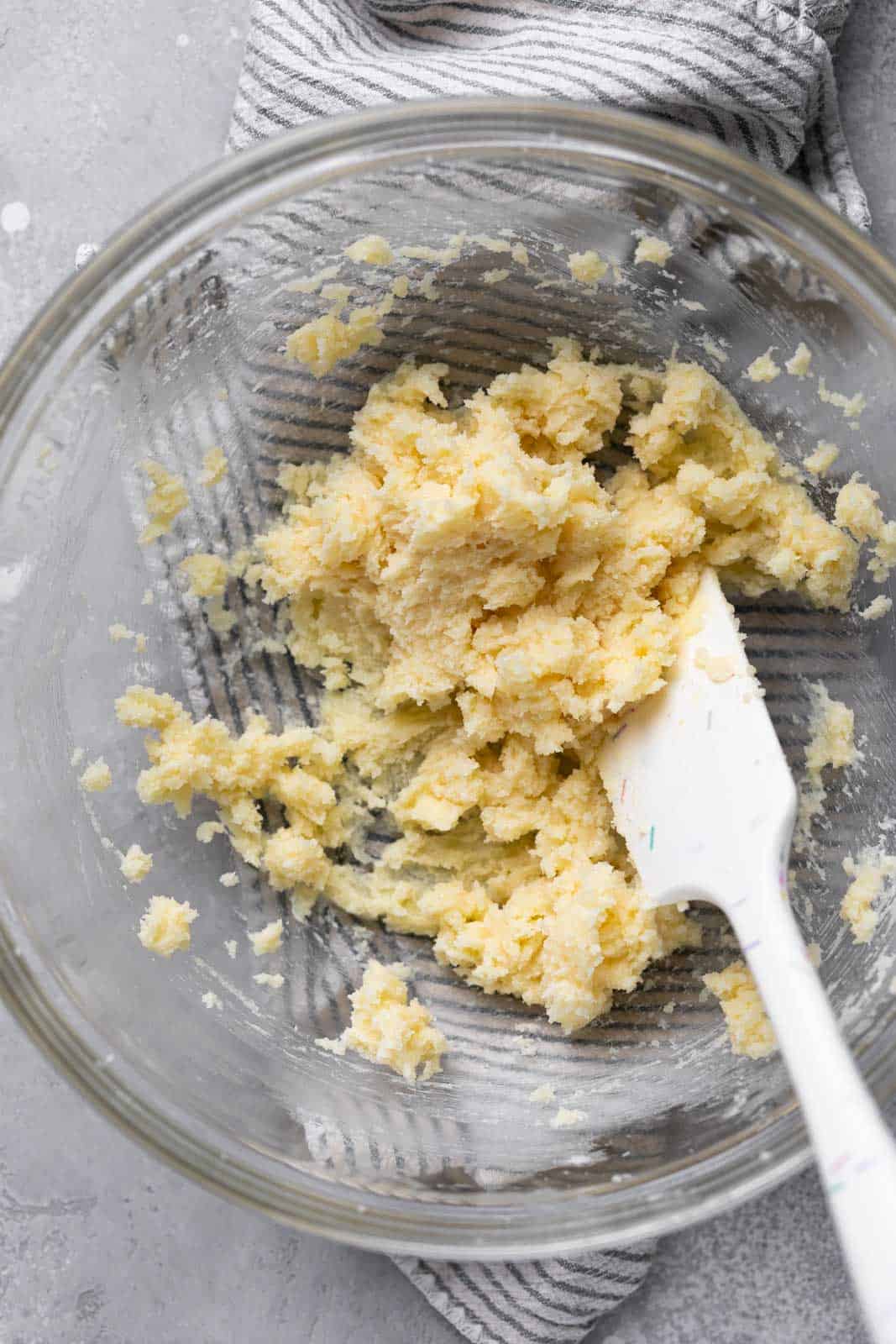 Creamed butter and sugar in a glass mixing bowl with a white spatula.