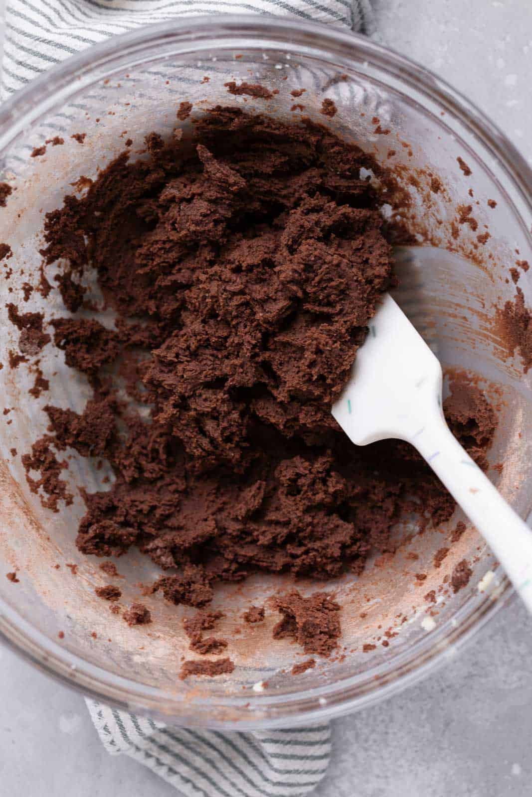 Edible chocolate cookie dough in a glass mixing bowl with a white spatula.