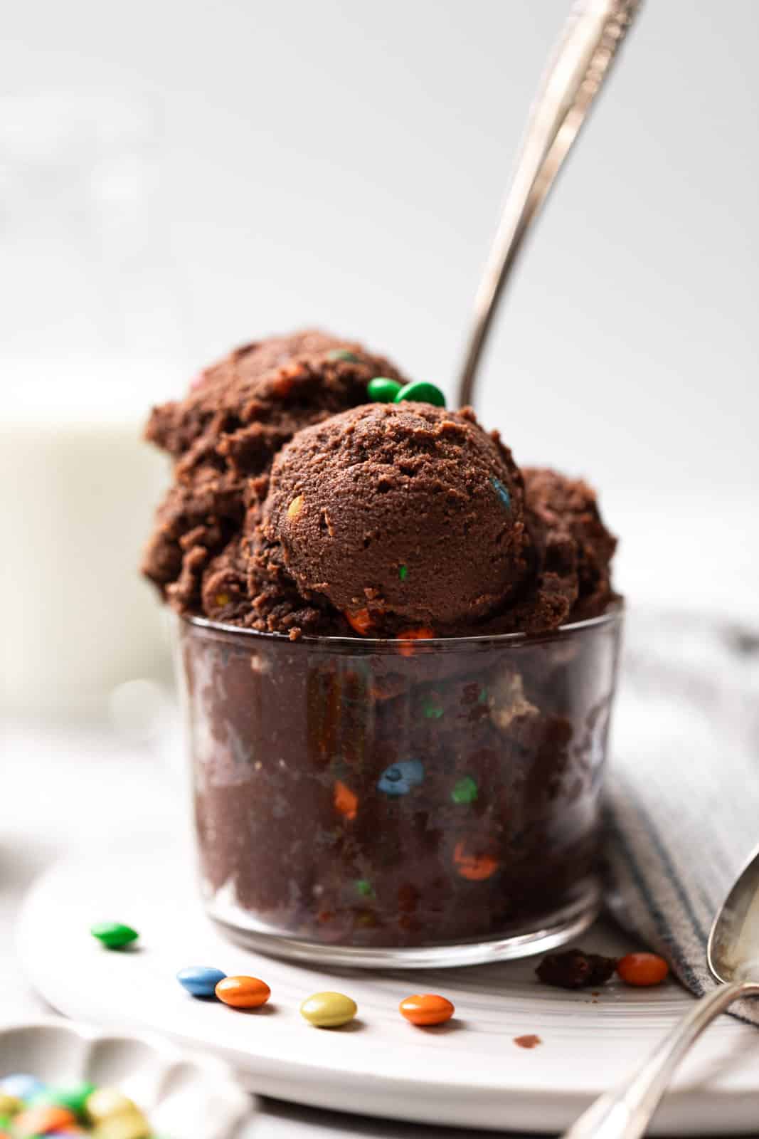 Scoops of edible chocolate cookie dough mixed with candy in a glass cup with a spoon.