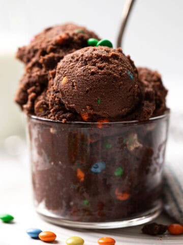 Scoops of edible chocolate cookie dough mixed with candy in a glass cup with a spoon.