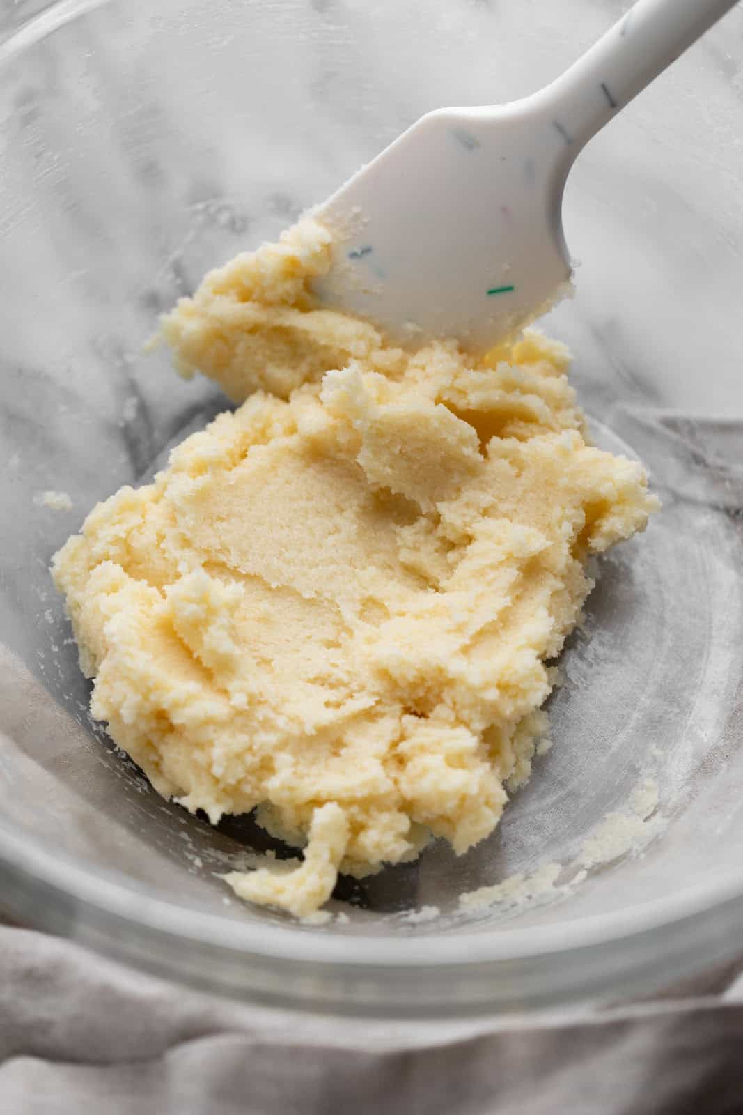 Creamed butter and sugar in a glass mixing bowl with a white spatula.