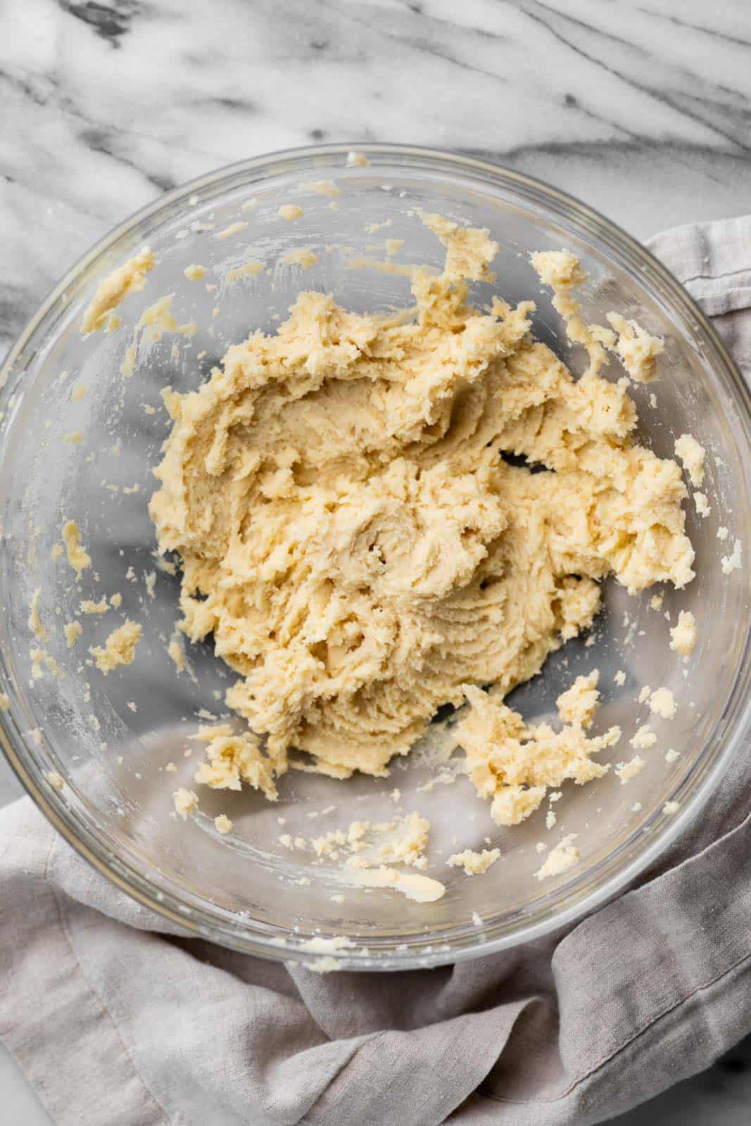 Creamed butter and sugar with heat treated flour mixed in, in a glass mixing bowl set on a flat surface.