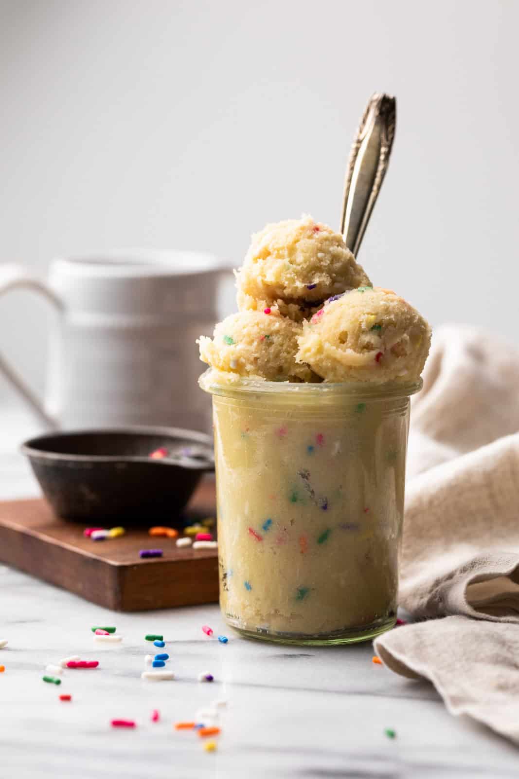 Glass jar filled with edible sugar cookie dough with scoops on top and a spoon inside.