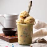 Glass jar filled with edible sugar cookie dough with scoops on top and a spoon inside.