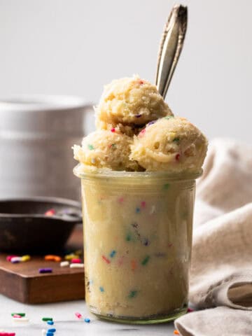 Glass jar filled with edible sugar cookie dough with scoops on top and a spoon inside.