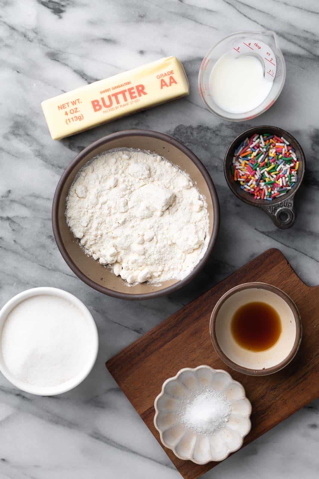 Edible sugar cookie dough ingredients in bowls set on a flat marble surface.