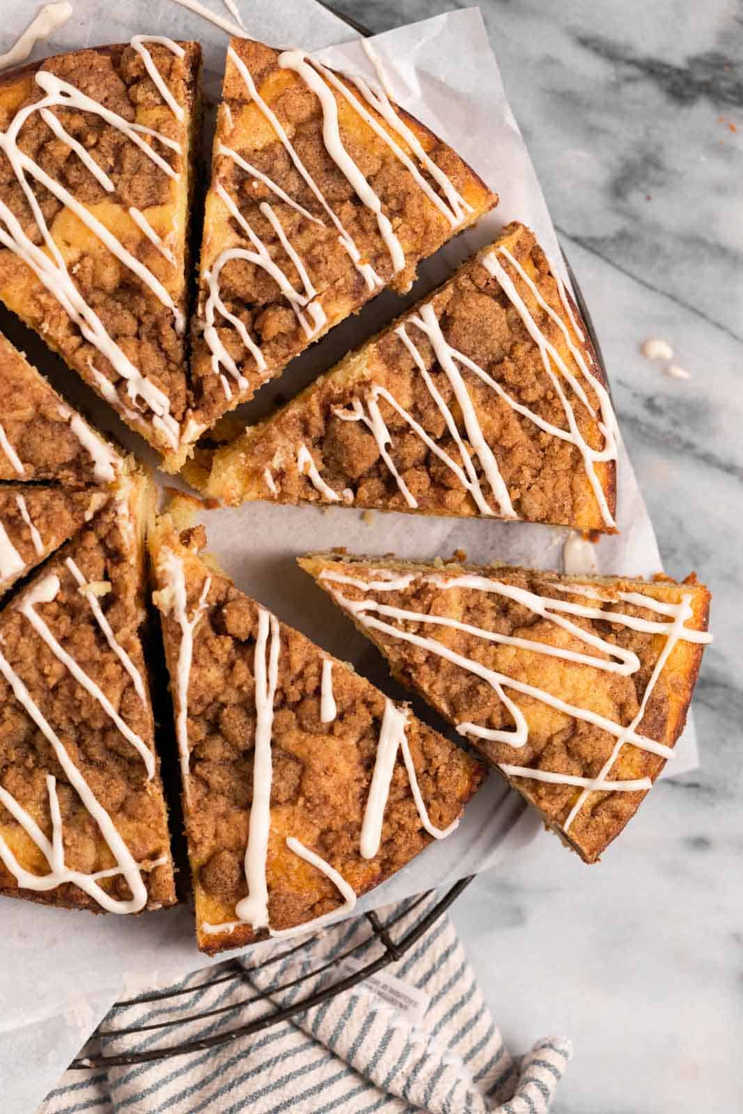 Overhead shot of sour cream coffee cake set drizzled with vanilla glaze set on parchment paper on a round wire rack and sliced into eight pieces.
