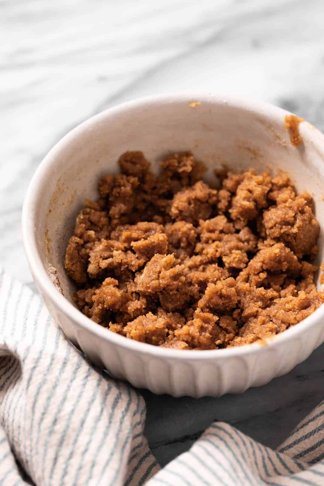 Mixed brown sugar crumble in a cream bowl set on a marble countertop with a linen.