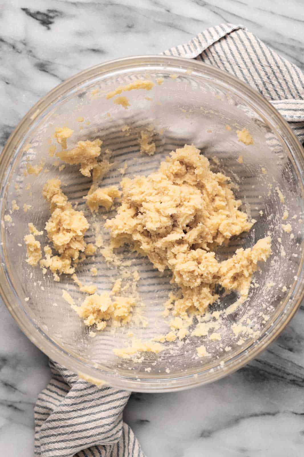 Creamed butter and sugar in a glass mixing bowl set on top of a striped linen on a marble surface.