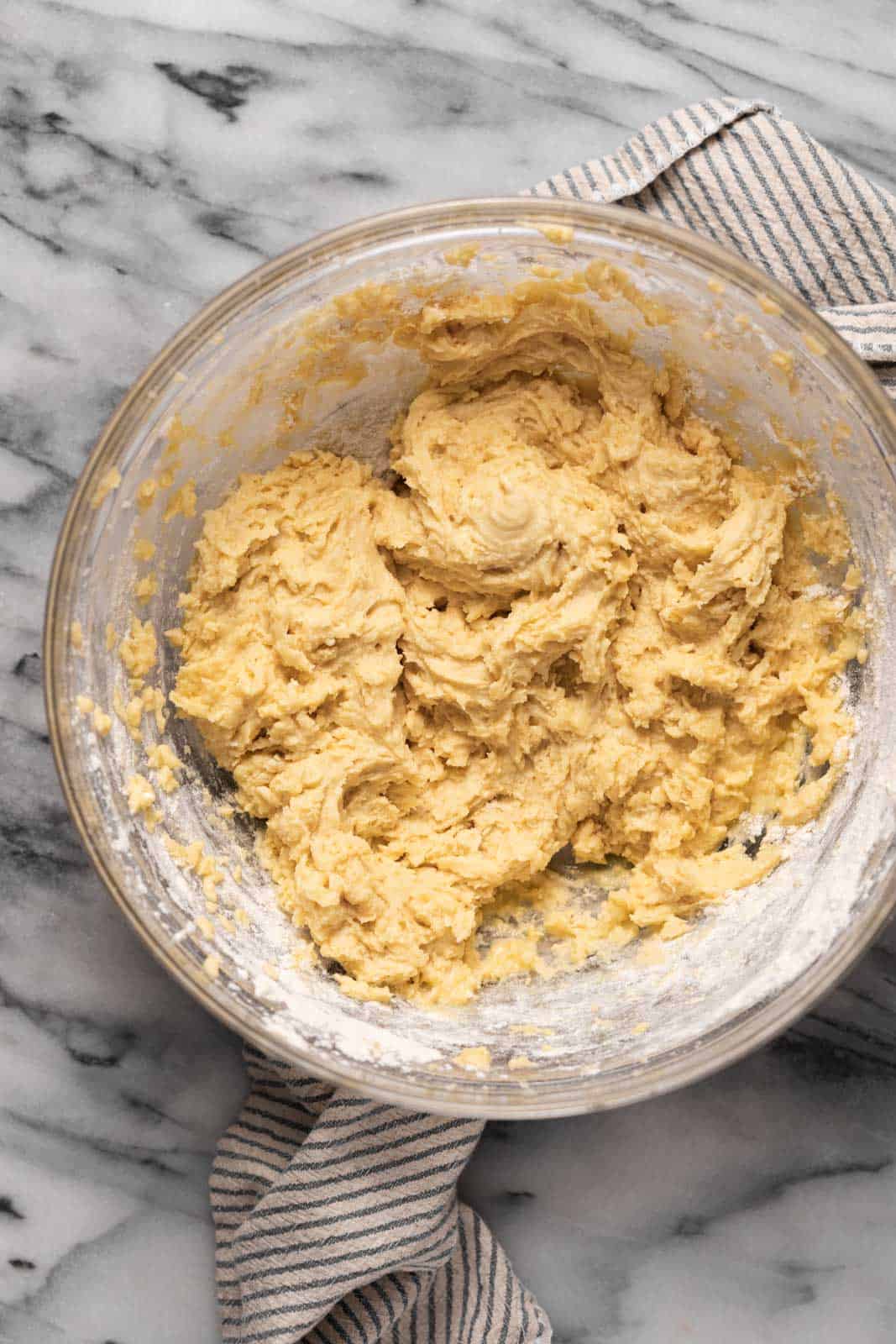Sour cream coffee cake batter mixing in a glass mixing bowl set on top of a striped linen on a marble surface.