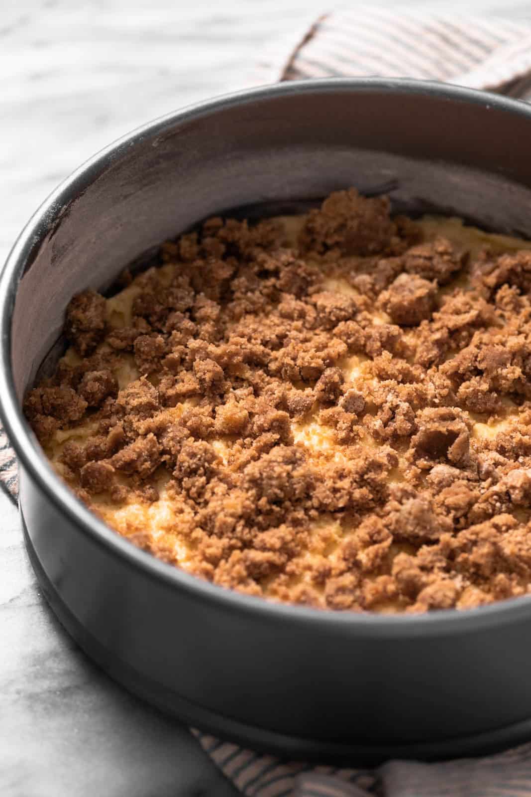Sour cream coffee cake layered with brown sugar crumble in a greased and floured springform pan set on a marble surface.